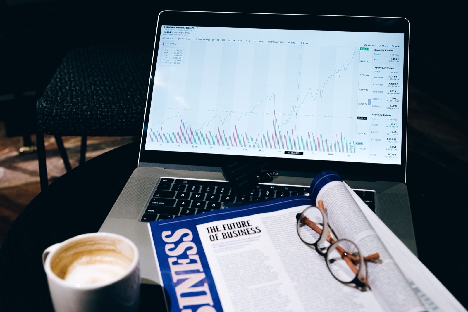 A working desk with market charts, a notebook and reading glasses